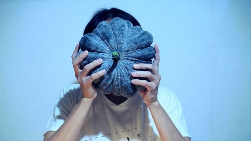 Woman with face covered by pumpkin against wall