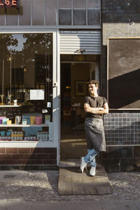 Male owner with legs crossed standing outside cafe on sunny day