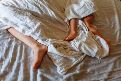 Upper view on elder child and smaller child feet in the parent's bed under bed sheet