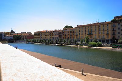 Buildings by canal against clear blue sky