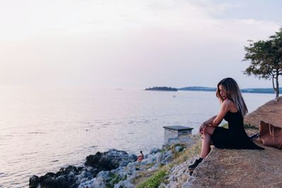 Portrait of young woman standing on rock by sea against sky