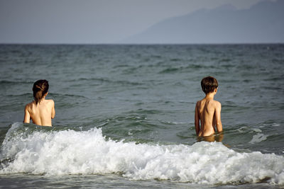 Shirtless siblings enjoying in sea against sky