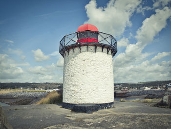 Lighthouse by street amidst buildings against sky