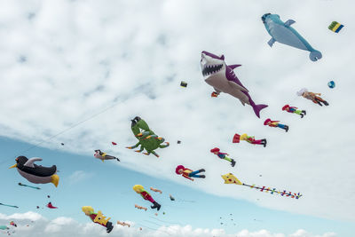 Low angle view of various colorful balloons flying against cloudy sky