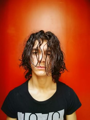 Portrait of serious teenage boy standing against red background