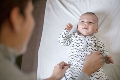 High angle view of mother adjusting baby boy clothing at home