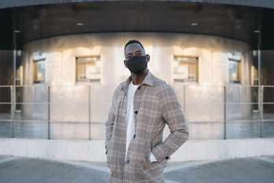Fashionable man with protective face mask standing against building