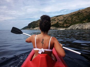 Rear view of woman kayaking in sea against sky