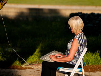 Woman typing in keyboard while sitting on chair against trees