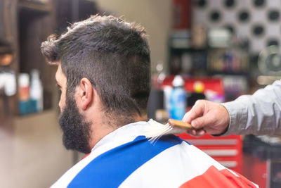 Cropped hand of barber cutting male customer hair in salon