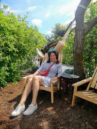 Portrait of woman sitting on chair against tree