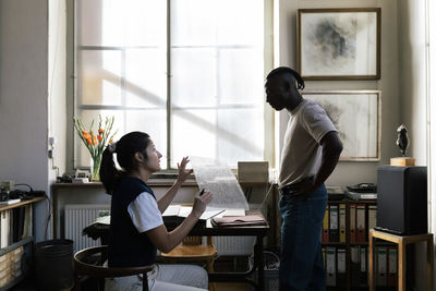 Female entrepreneur discussing over building material sample with male colleague in workshop