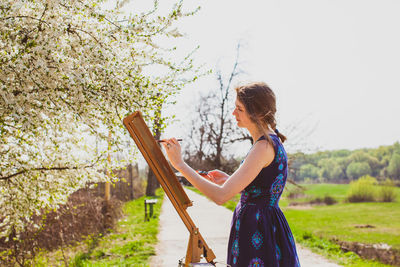 Side view of woman standing by plants against sky