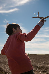 Rear view of boy playing with model airplane on land against sky