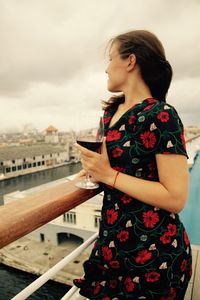 Young woman having drink while standing by railing