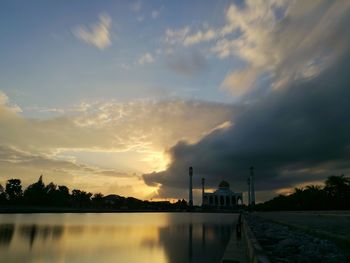 Scenic view of lake by buildings against sky during sunset