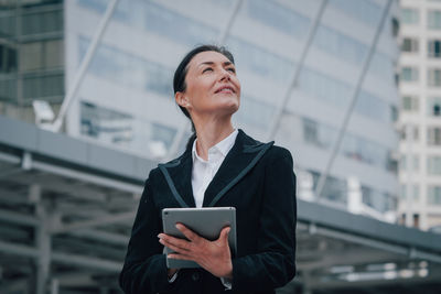 Businesswoman using digital tablet while standing by office building exterior