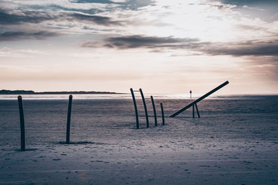 Wooden posts on beach against sky during sunset