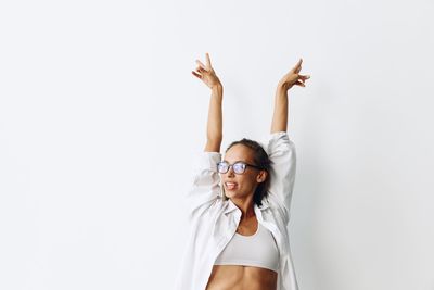 Young woman with arms raised standing against white background