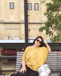 Young woman sitting on bench against building