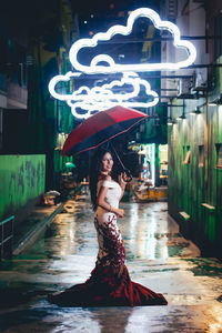 Portrait of woman holding umbrella while standing at night