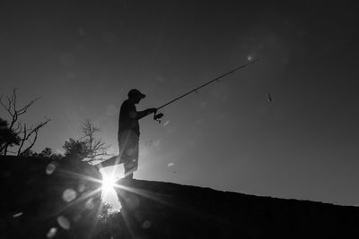 Silhouette man holding umbrella against bright sun