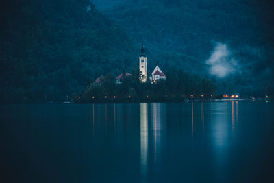 Illuminated building by lake against sky at night