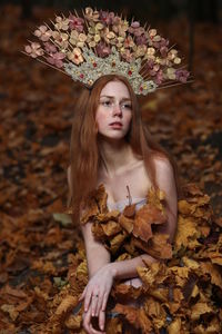 Thoughtful young woman wearing flowers on hair sitting at forest during autumn