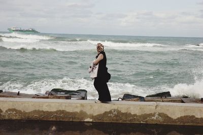 Side view of woman walking on retaining wall by sea