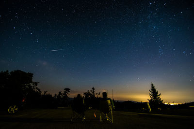 Rear view of friends sitting on chairs against star field