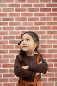 Portrait of cute girl standing against brick wall