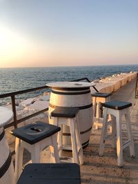 Chairs and table at beach against clear sky during sunset