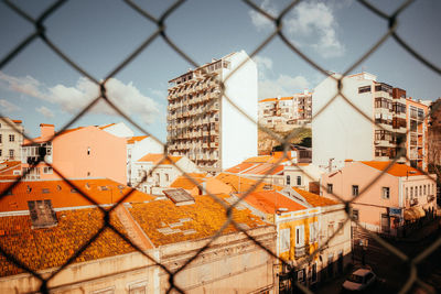 Buildings against sky seen through chainlink fence