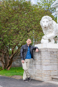 A man in casual clothes stands near a beautiful white building with lions person