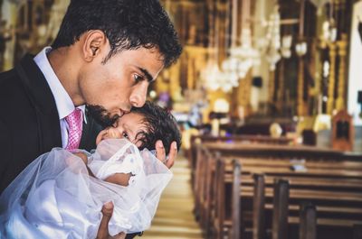 Young man kissing baby girl on forehead in church