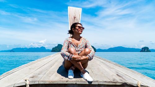 Full length of smiling young woman sitting on beach against sky