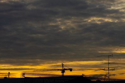 Silhouette construction side against dramatic sky during sunset