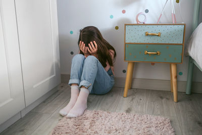 Unrecognizable little girl covering her face with hands sitting on the floor