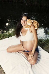 Portrait of smiling pregnant woman with toy siting at lakeshore