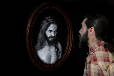 Digital composite image of man looking at angry reflection in mirror against black background