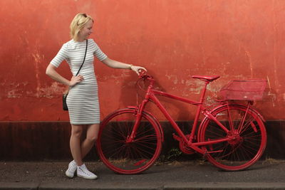 Full length of woman holding red bicycle while standing against wall