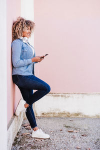 Portrait of smiling hispanic woman with afro hair in city using mobile phone and headset. lifestyle