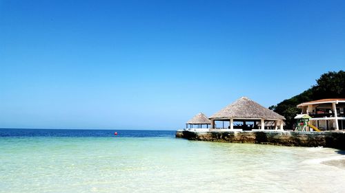 View of built structure by sea against clear blue sky