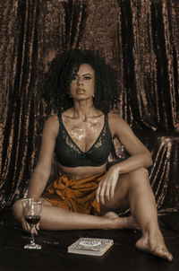 Portrait of young woman with wine sitting against wall