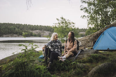 Smiling senior women talking to each other while sitting on rock during camping