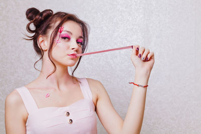 Young woman with pink make-up chewing gum against wall