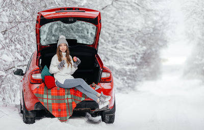 Portrait of woman sitting on snow covered car