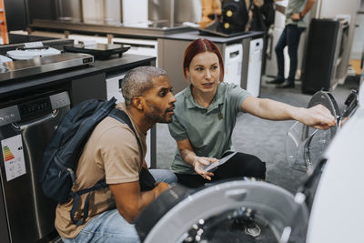 Saleswoman advising male customer in buying washing machine at appliances store