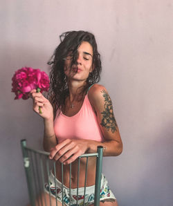 Beautiful woman standing by pink flowering plant against wall