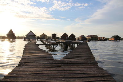 Pier amidst houses by sea against sky during sunset